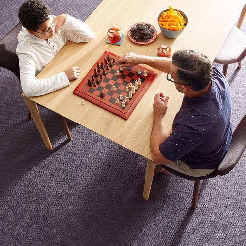 Father is playing chess with son on a gray carpet floor from Michaels Carpets Huntington Beach in Huntington Beach, CA